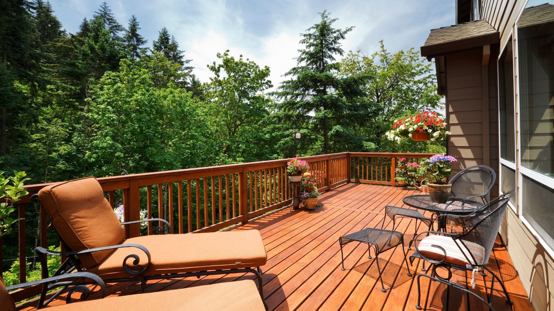 A cozy wooden deck in Rockford, IL, featuring chairs, loungers, and vibrant potted plants.