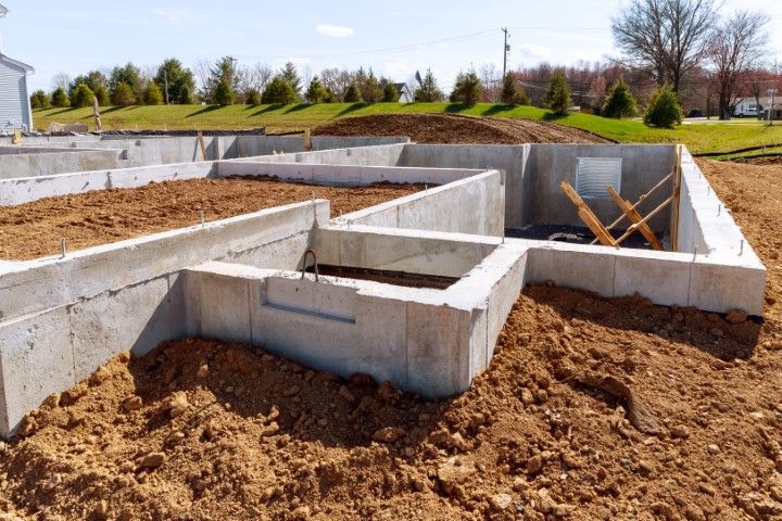 Concrete foundation walls at a construction site with dirt mounds and open lots in the background