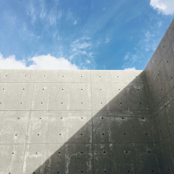 Concrete wall and blue sky with a sharp diagonal shadow.