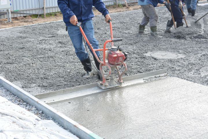 Workers smoothing wet concrete with a red power trowel on a construction site
