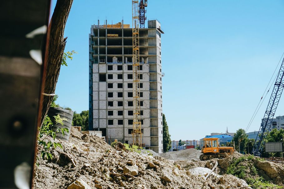 Construction site with a tall unfinished concrete building, rubble in foreground, and blue sky overhead