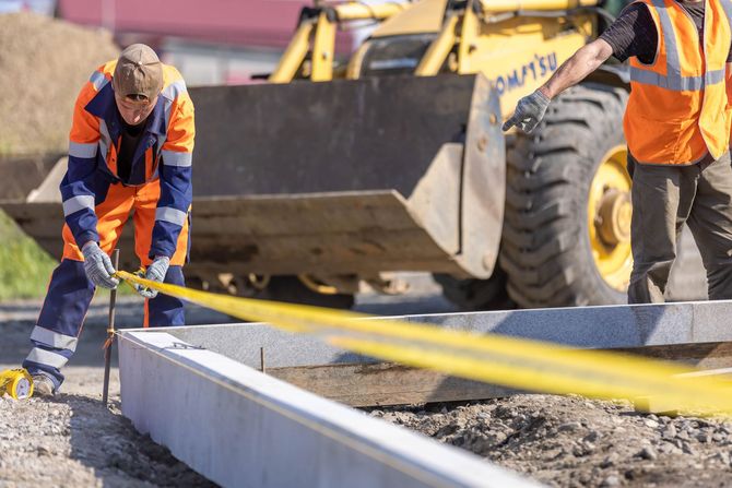 Construction workers smoothing concrete curb beside a yellow loader on a roadwork site