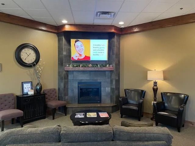 Cozy waiting area with fireplace, TV, seating, and a clock.