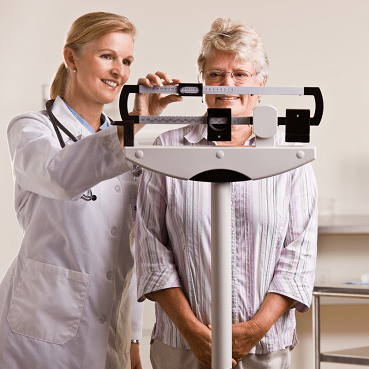 Elderly woman on a scale assisted by a doctor.