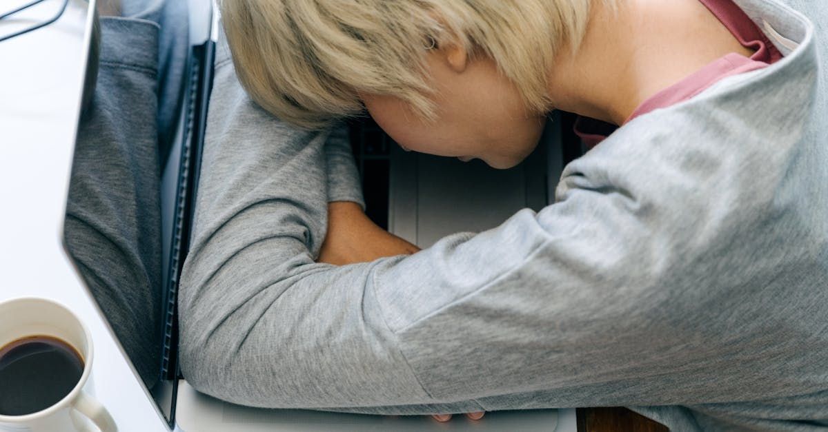 A woman is sleeping on a desk next to a cup of coffee.