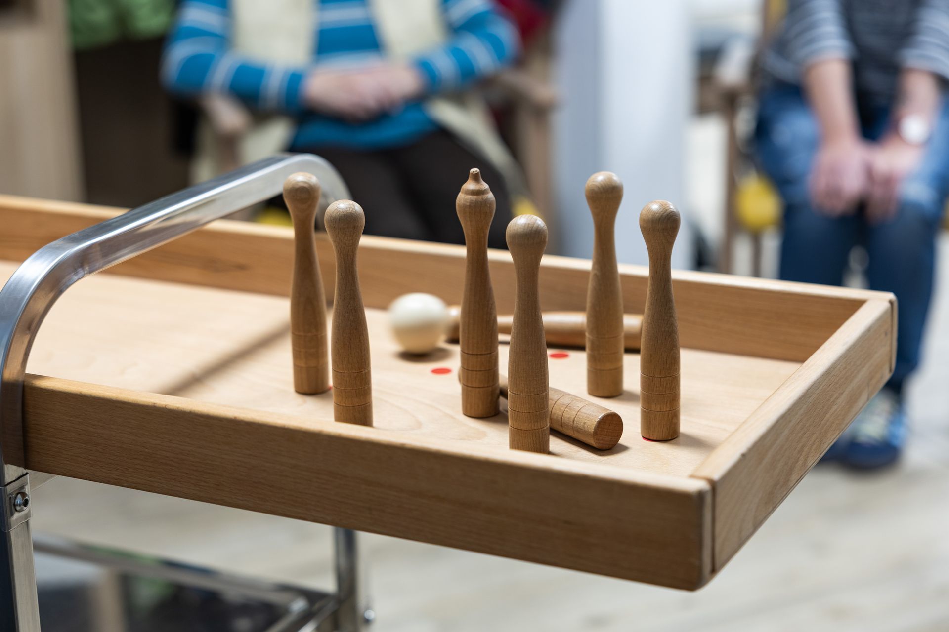Ein hölzernes Kegelspiel mit Kegeln und einer Kugel, gespielt in einem Innenraum.