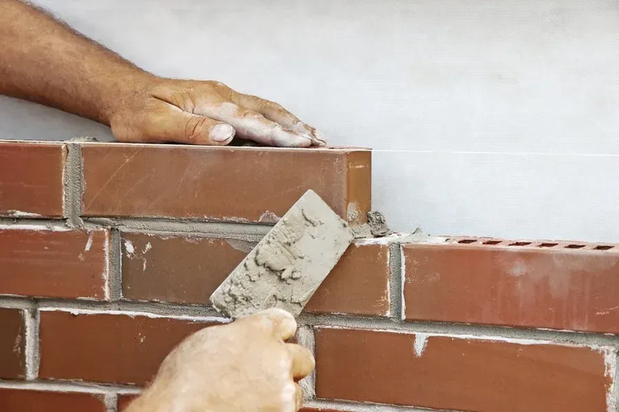 Hands using a trowel to apply mortar on a brick wall under construction