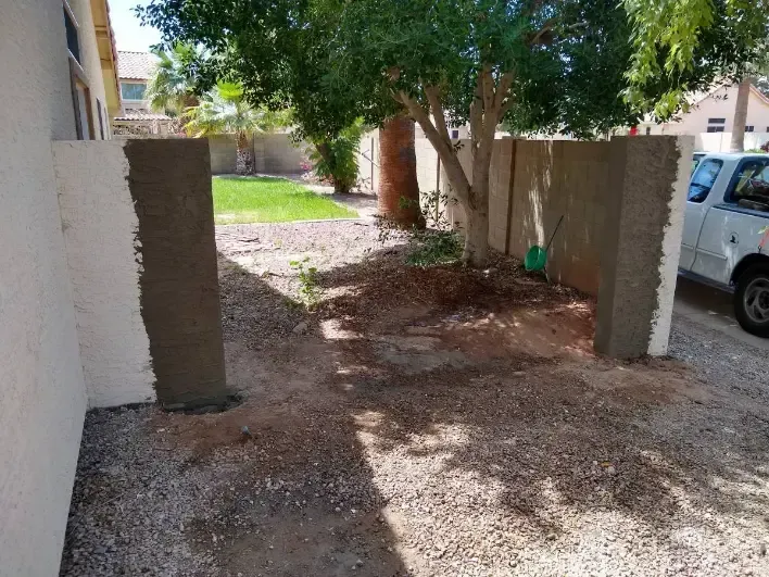 Narrow dirt walkway between walls with a tree ahead and a parked white van on the right