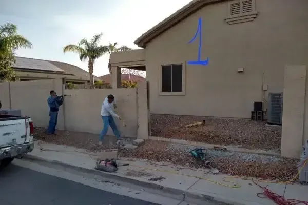 Workers installing landscaping in front of a beige house with gravel and a palm tree.