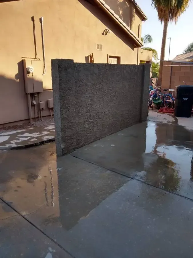 Outdoor wet concrete patio with a dark gray privacy wall beside a house