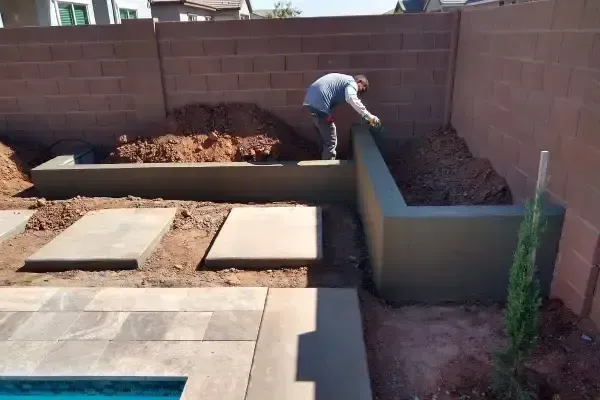 Backyard with raised concrete planters and a person working in a dirt bed near a wall
