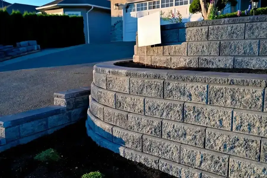 Curved stone retaining wall beside a driveway in a residential neighborhood at dusk