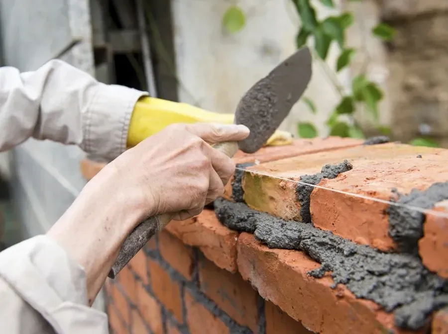 Hands applying mortar with a trowel while building a brick wall outdoors