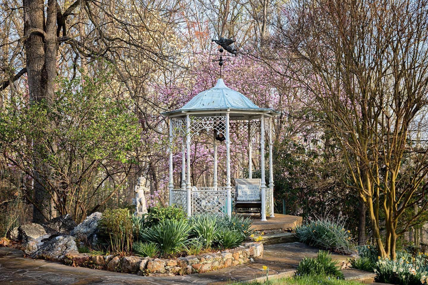 A white wrought-iron gazebo sits in a garden.