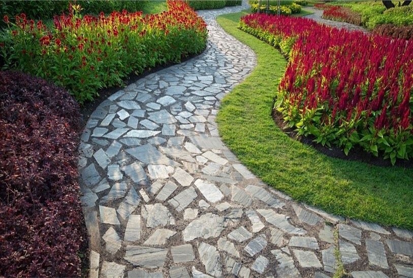 A stone pathway curves through a garden bordered by vibrant red.