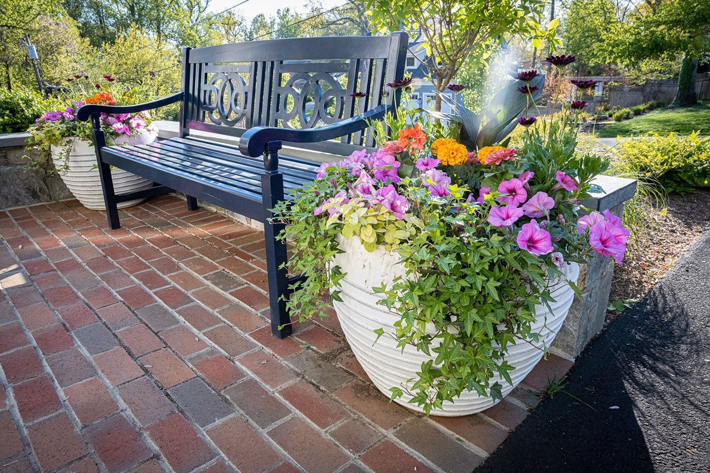 A dark metal bench sits on a brick patio next to a large.