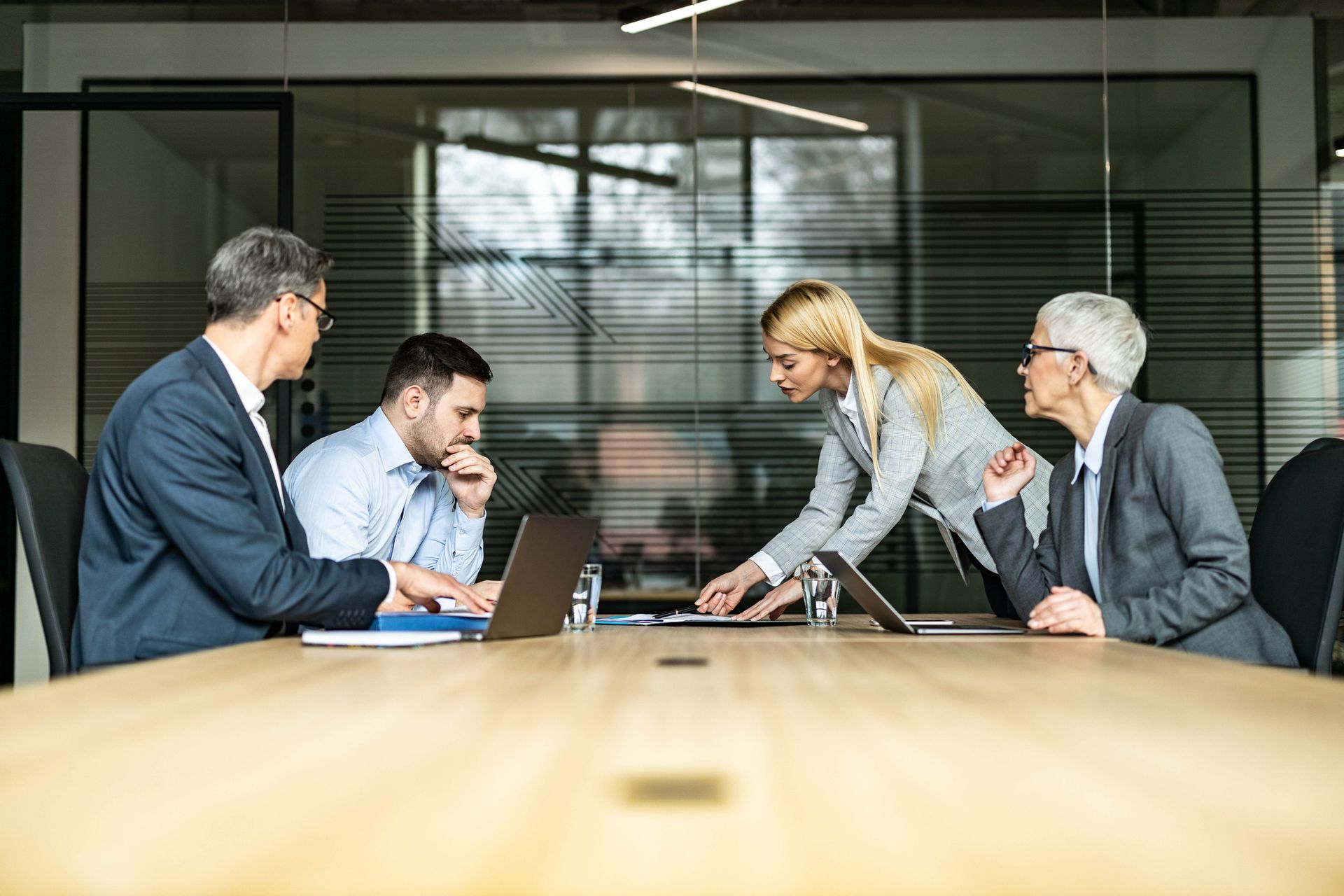 A group of business people are sitting around a conference table with laptops.