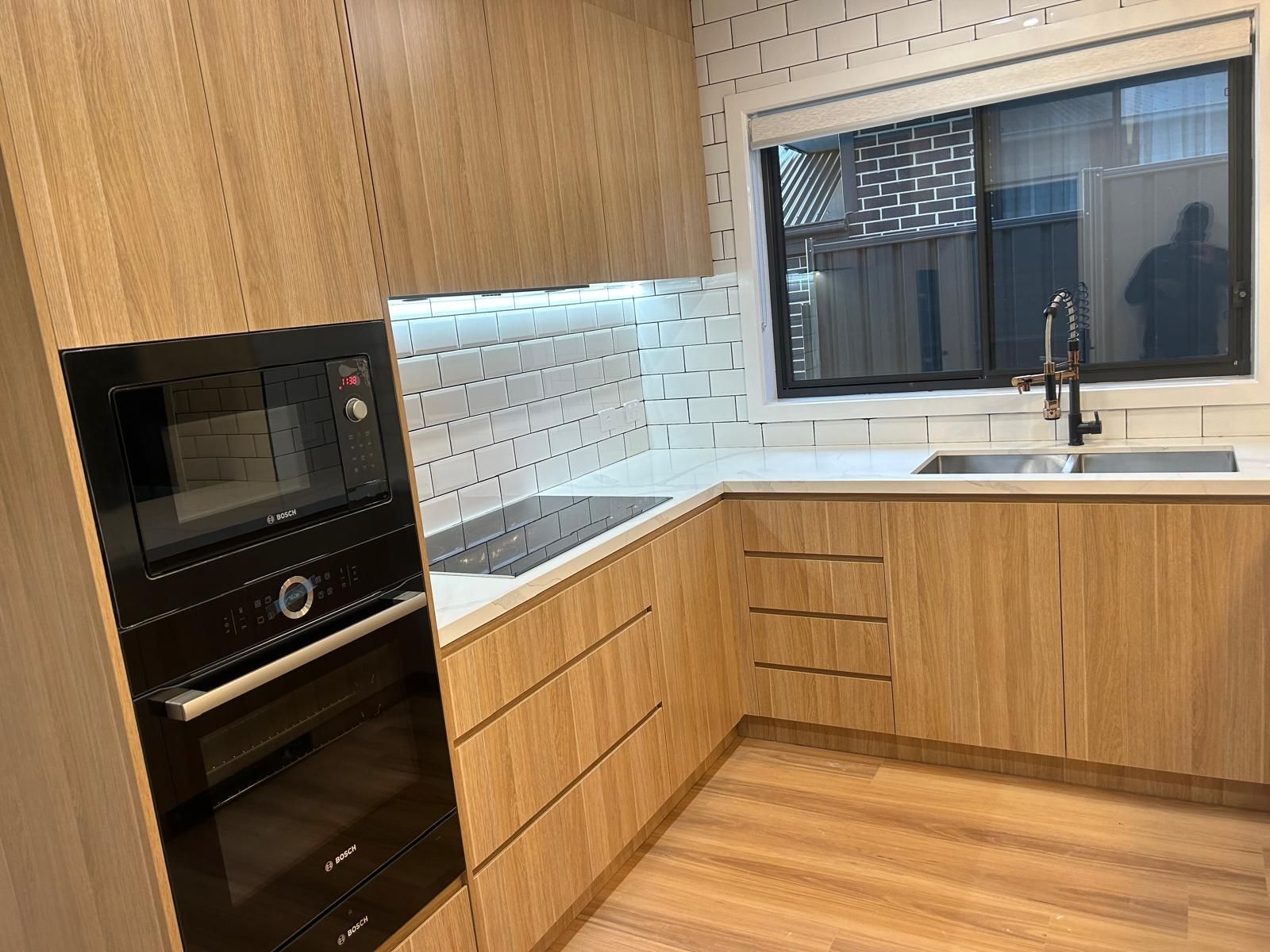 A kitchen with wooden cabinets , a black oven , a sink , and a window.