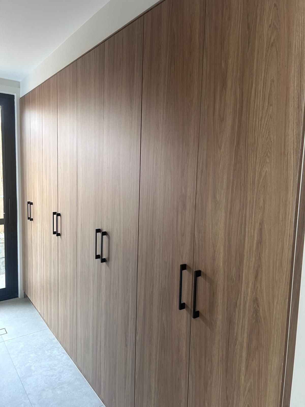 A row of wooden cabinets with black handles in a hallway.