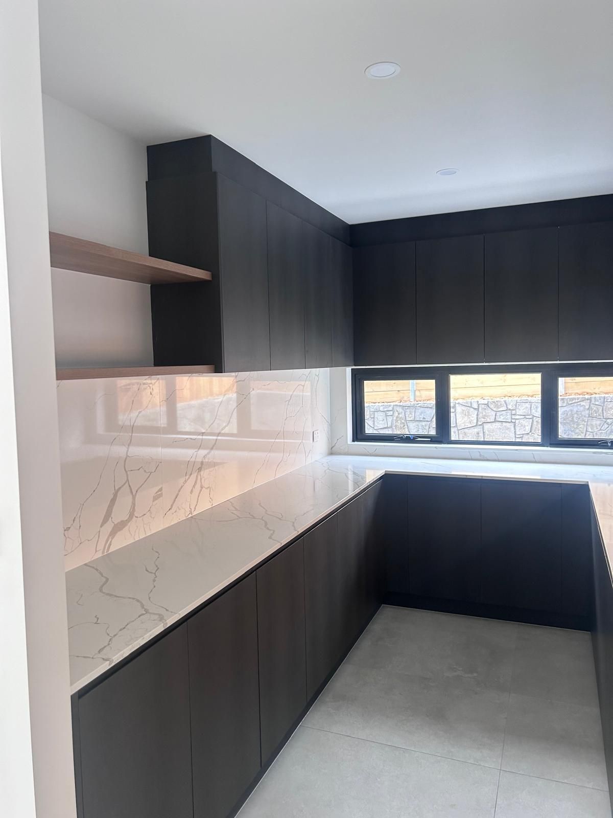 A kitchen with black cabinets and white counter tops and a window.