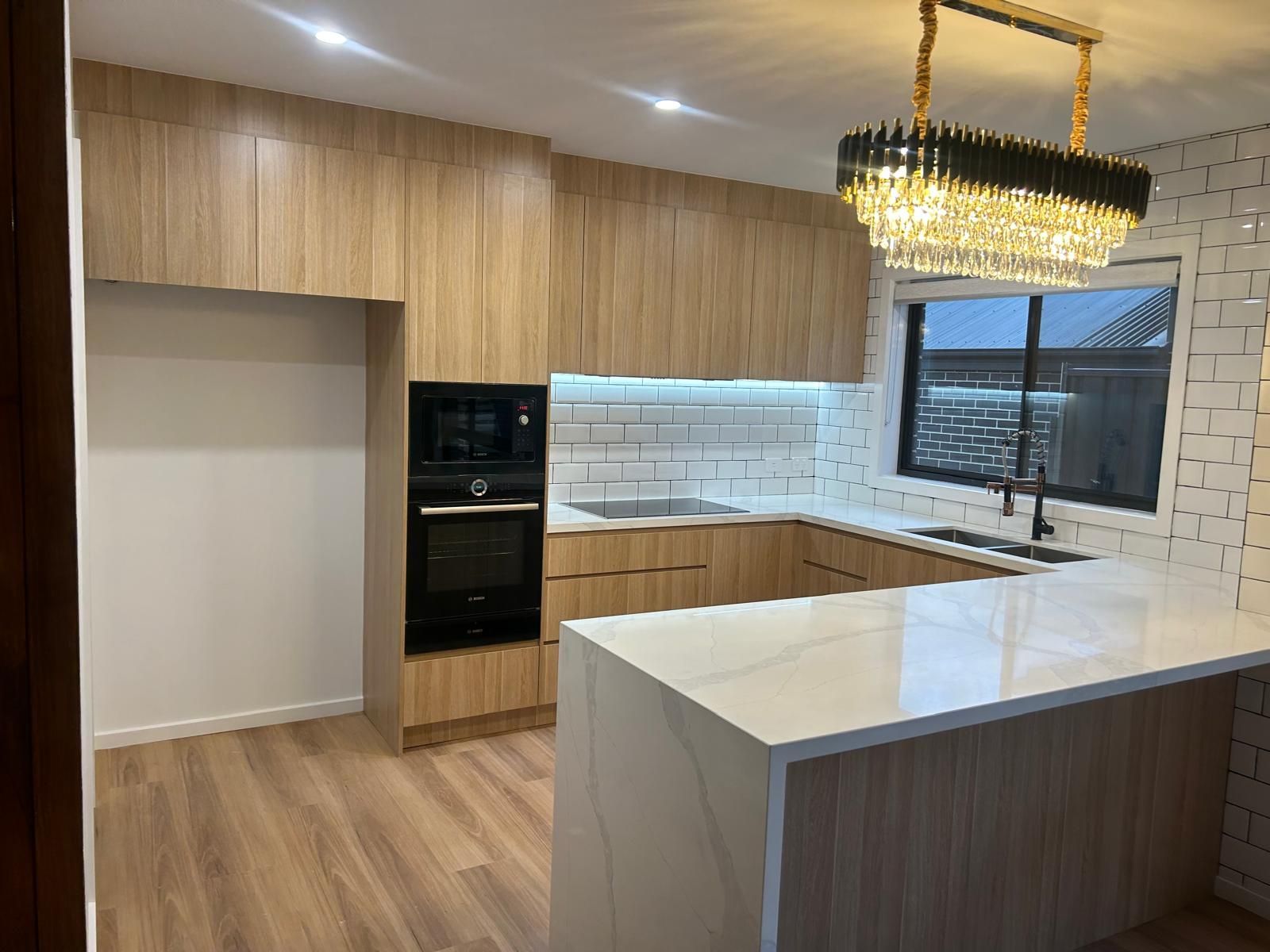A kitchen with wooden cabinets , white counter tops , and a chandelier hanging from the ceiling.