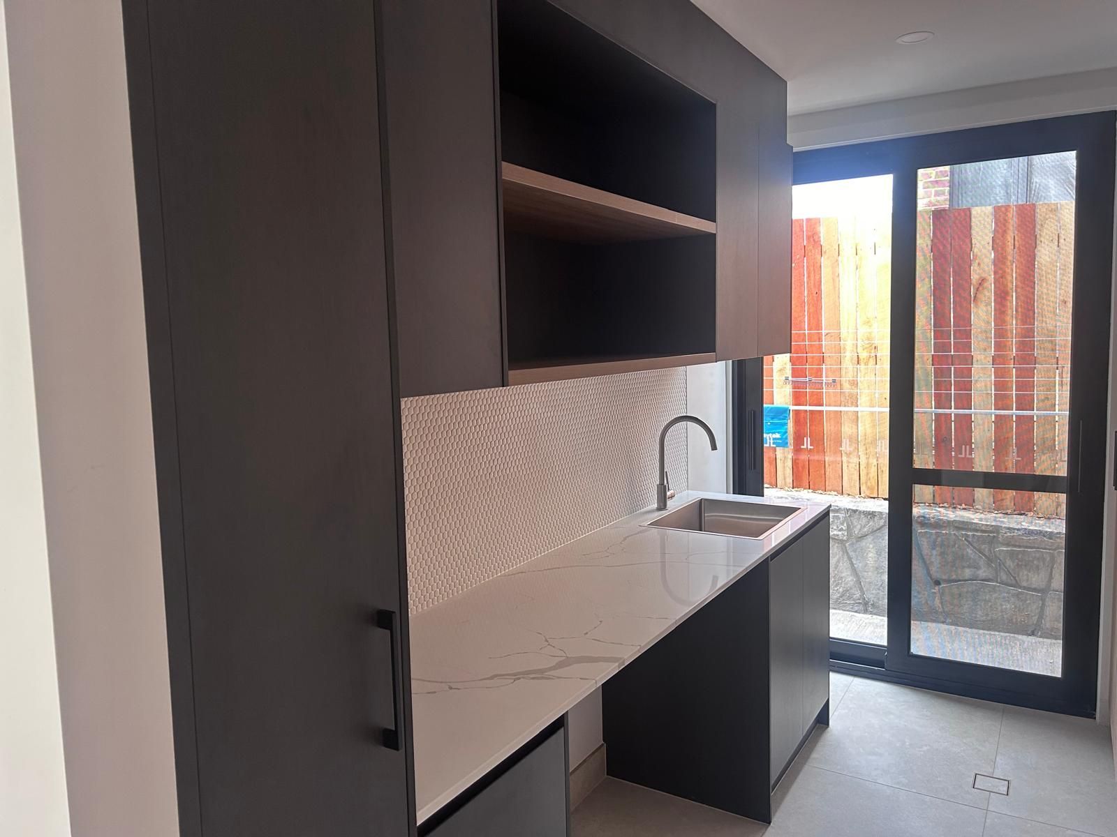 A kitchen with black cabinets , a sink , and a large window.