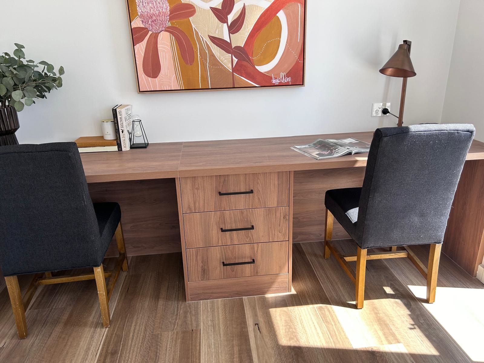 Two chairs are sitting at a desk in a room with a painting on the wall.