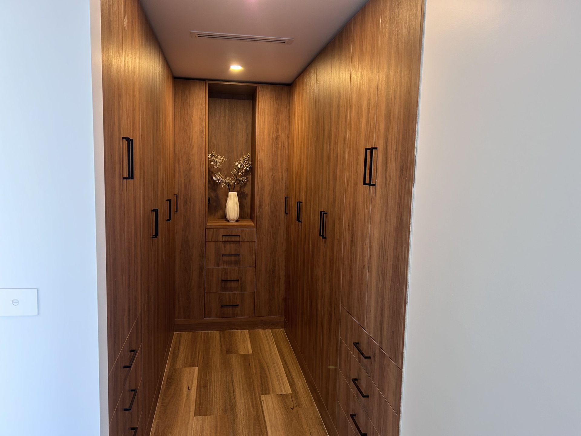 A walk in closet with wooden cabinets and drawers.