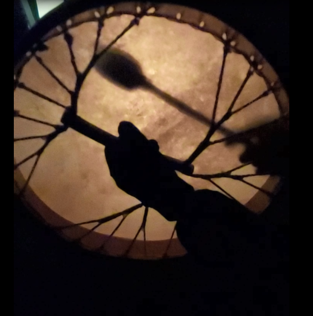 Silhouette einer Hand, die einen Trommelschlägel hält und auf eine große runde Trommel schlägt.