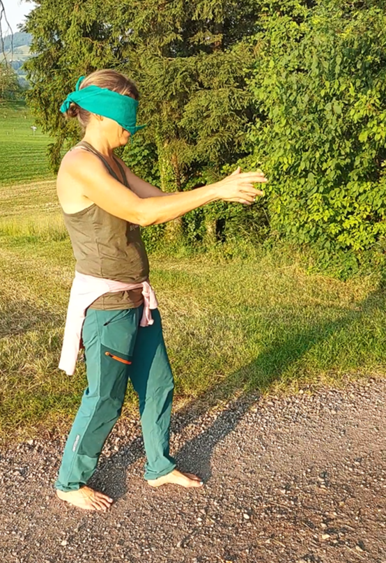 Frau mit verbundenen Augen und ausgestreckten Armen geht im Freien.  grüner Wald. Sonniger Tag.