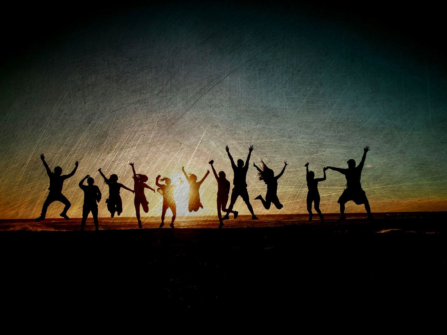 Eine Gruppe springt mit erhobenen Armen vor dem Hintergrund eines Sonnenuntergangs.