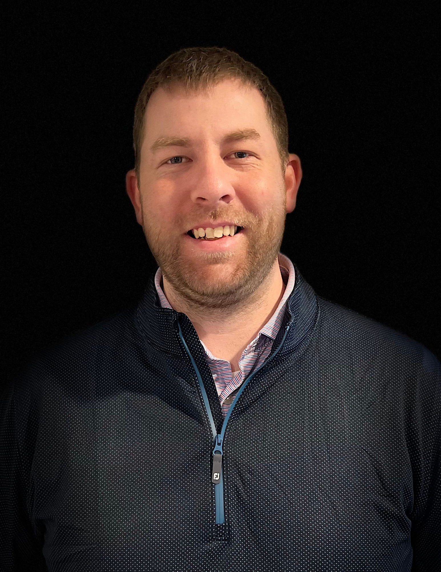 A man with a beard is wearing a blue jacket and smiling.