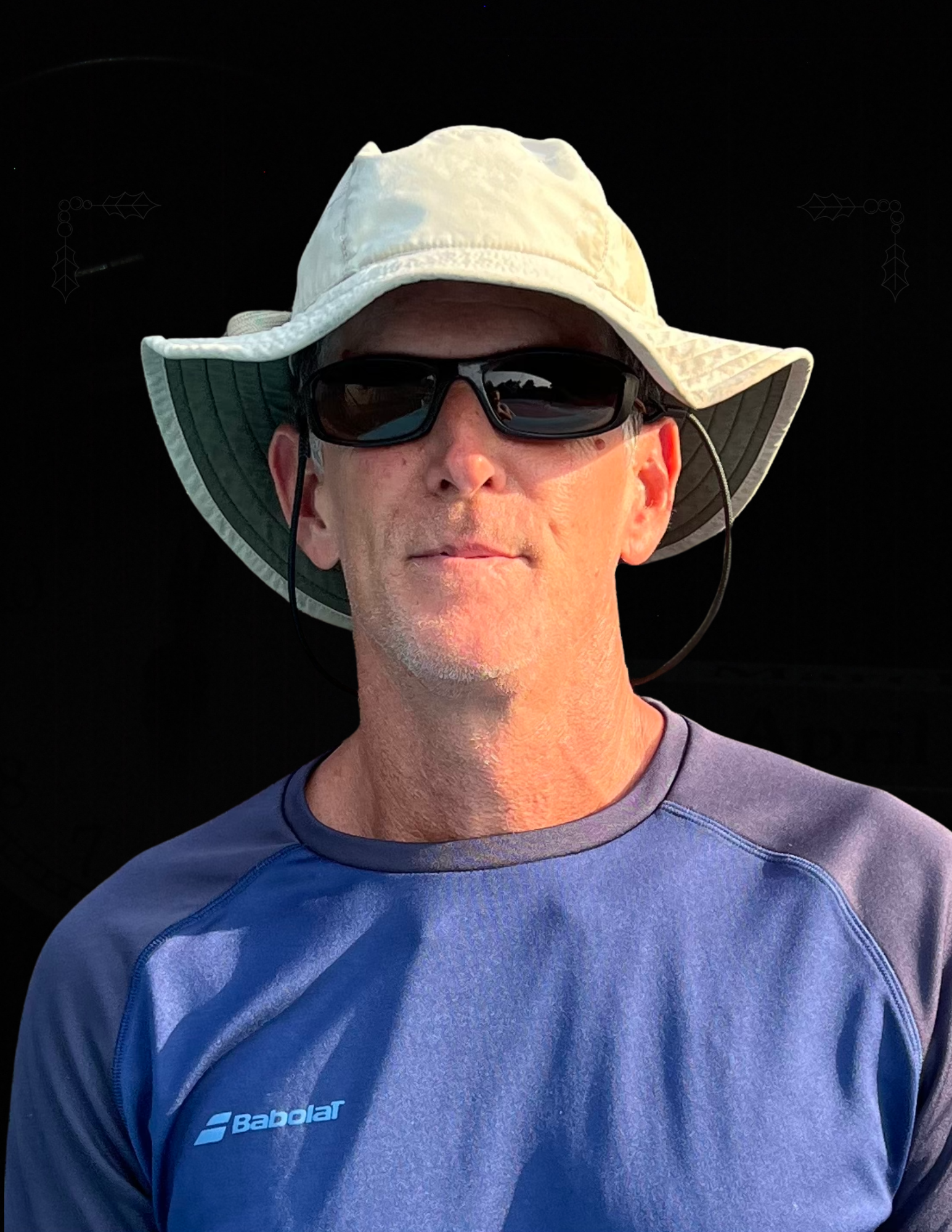 A man wearing a hat and sunglasses is standing in front of a black background.