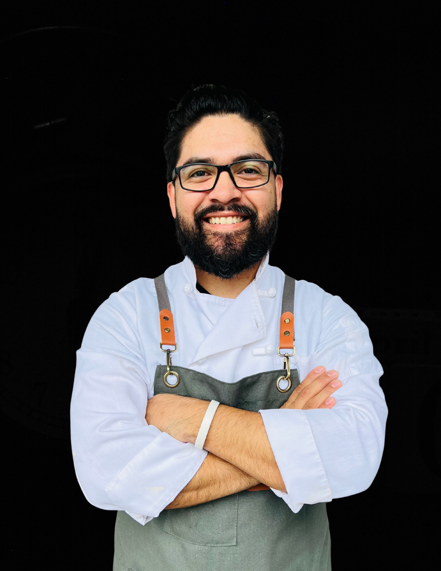 A man with a beard and glasses is wearing an apron and smiling with his arms crossed.
