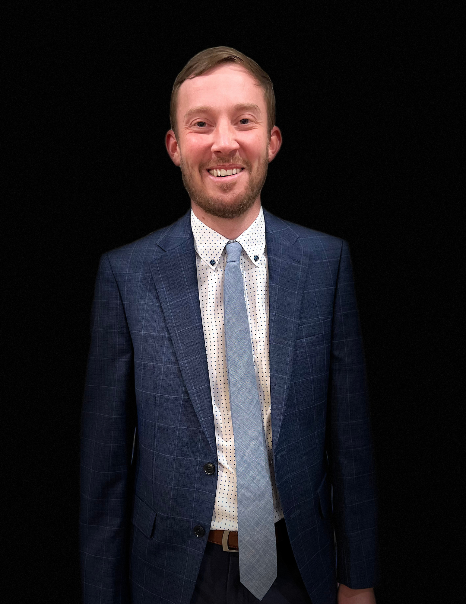 A man in a suit and tie is smiling in front of a black background.