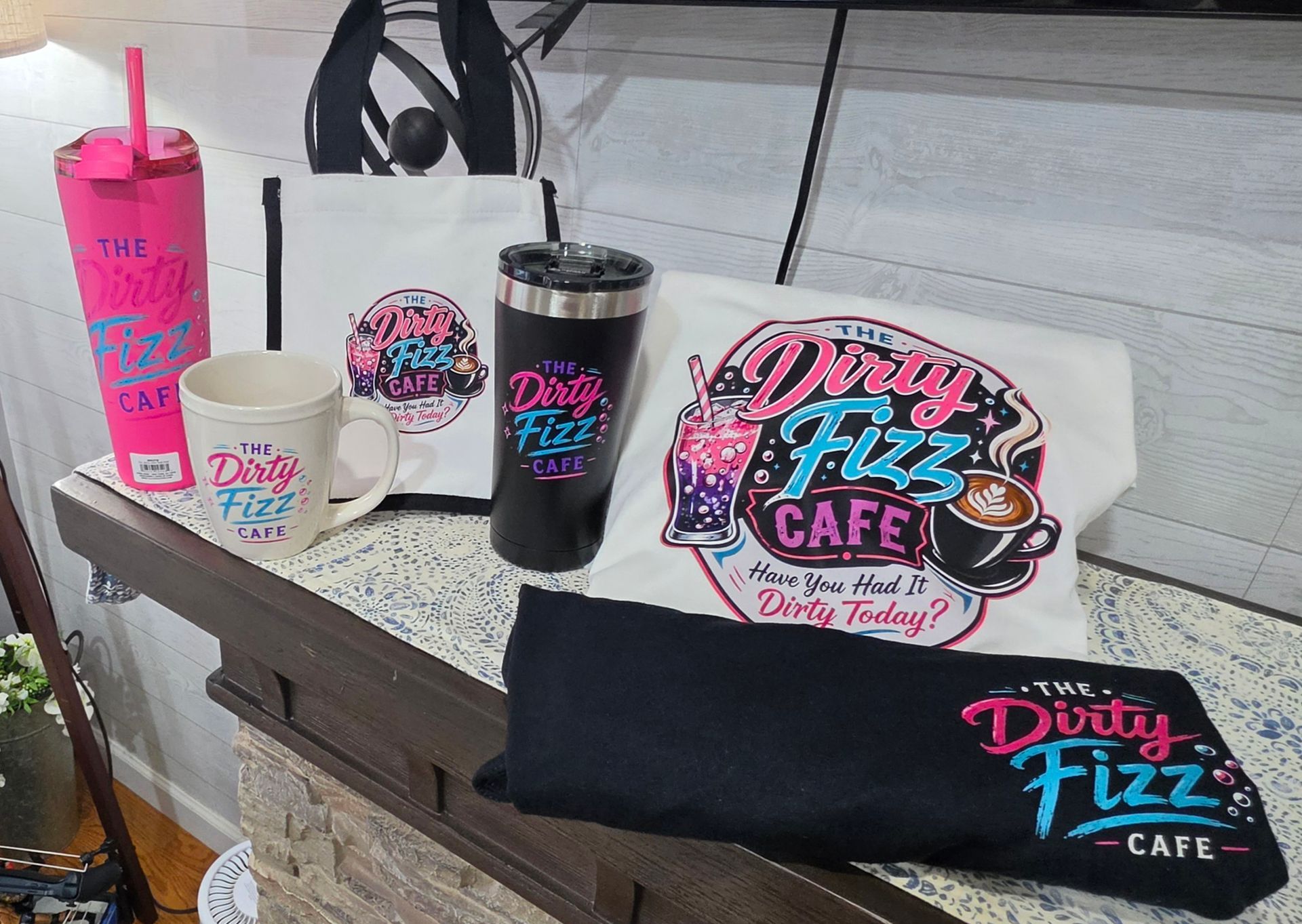 Branded Dazy Fizz Cafe drinkware and merch displayed on a table outdoors