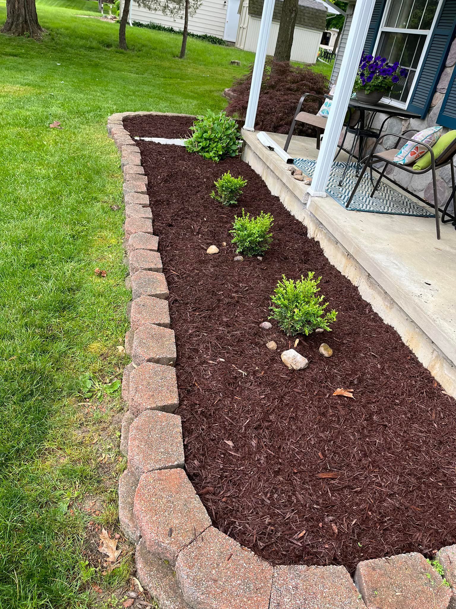 A garden bed with plants and mulch on the side of a house.