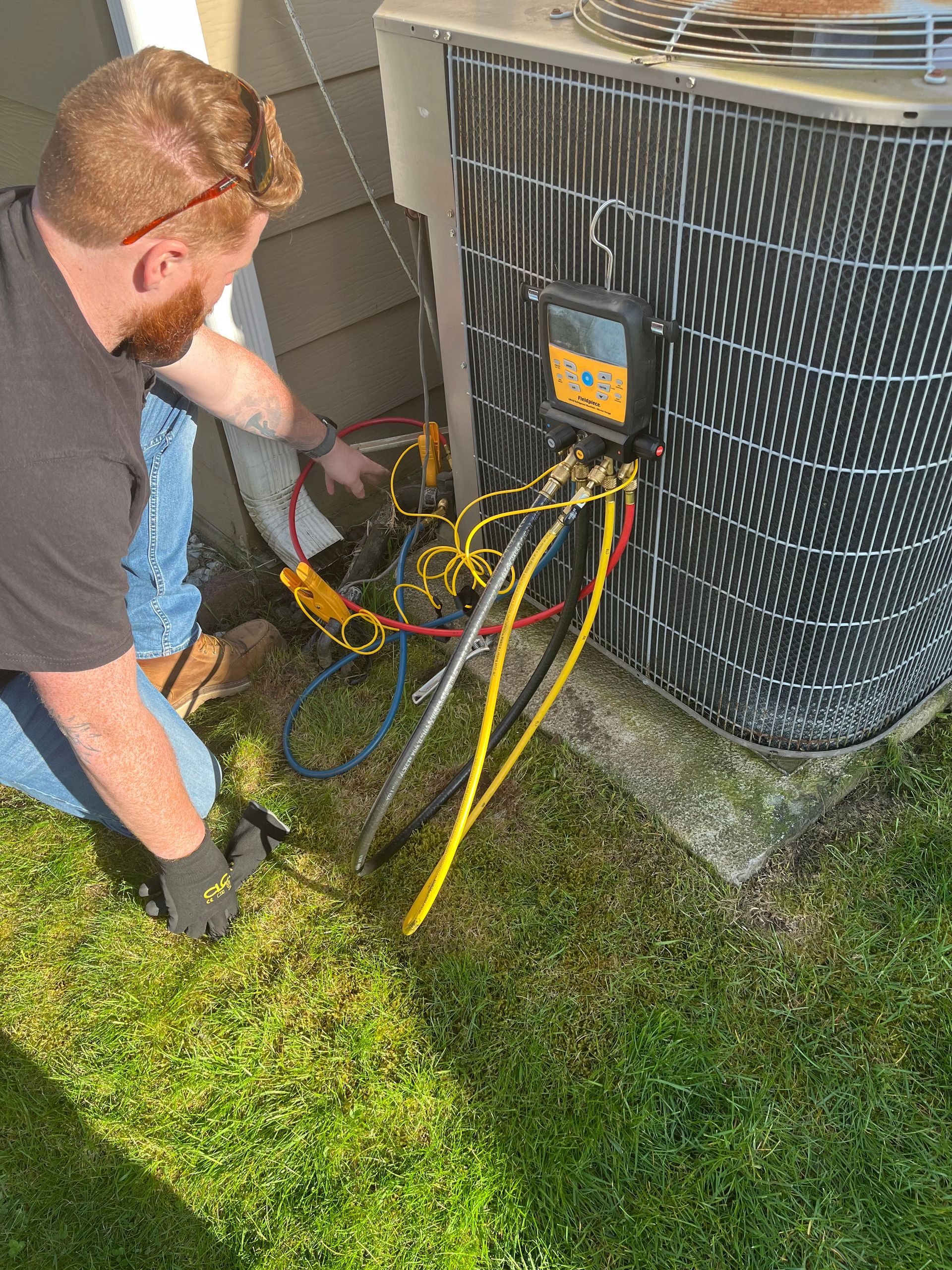 A man is working on an air conditioner outside in the grass.