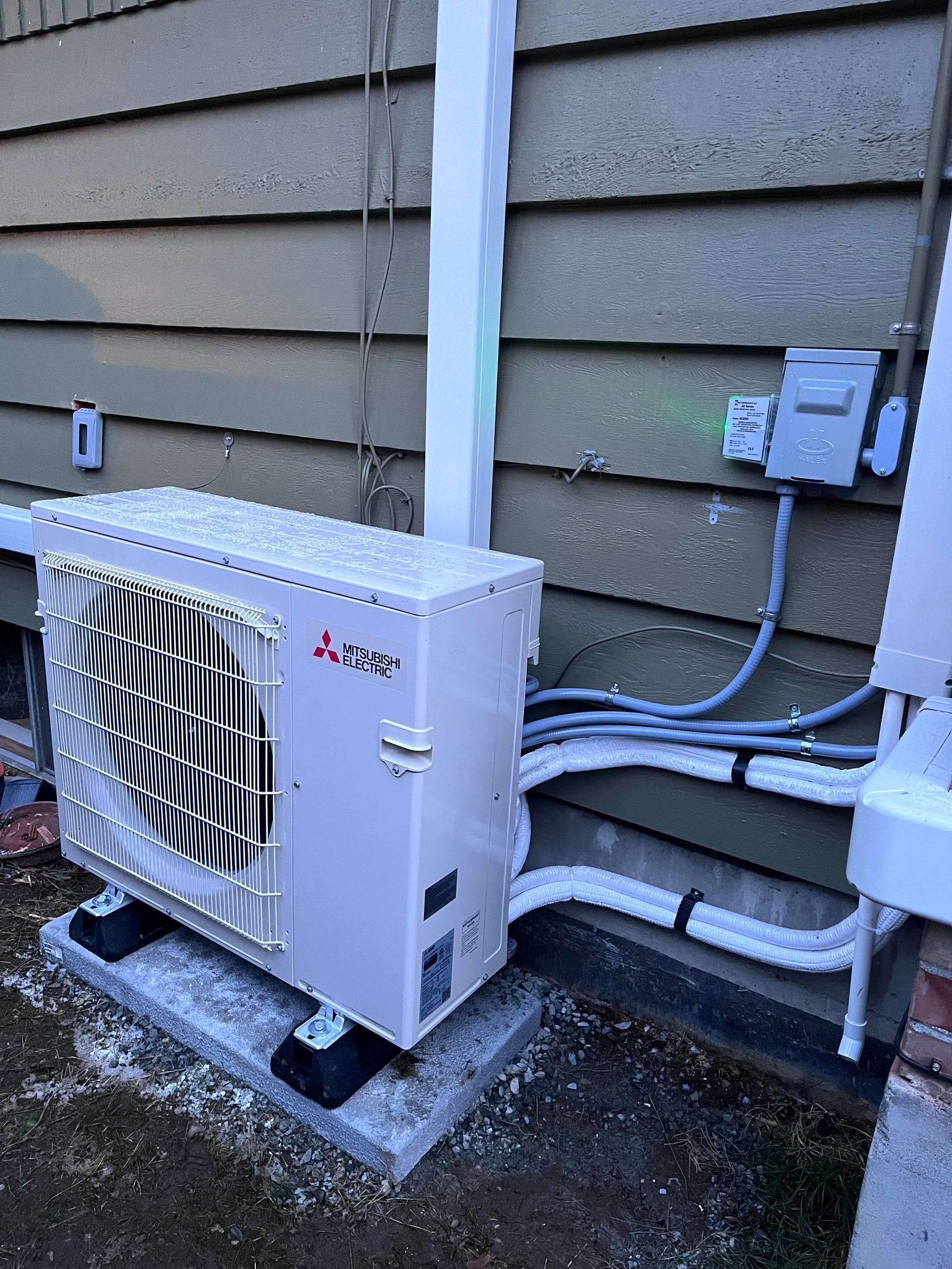 A white air conditioner is sitting on the side of a house.