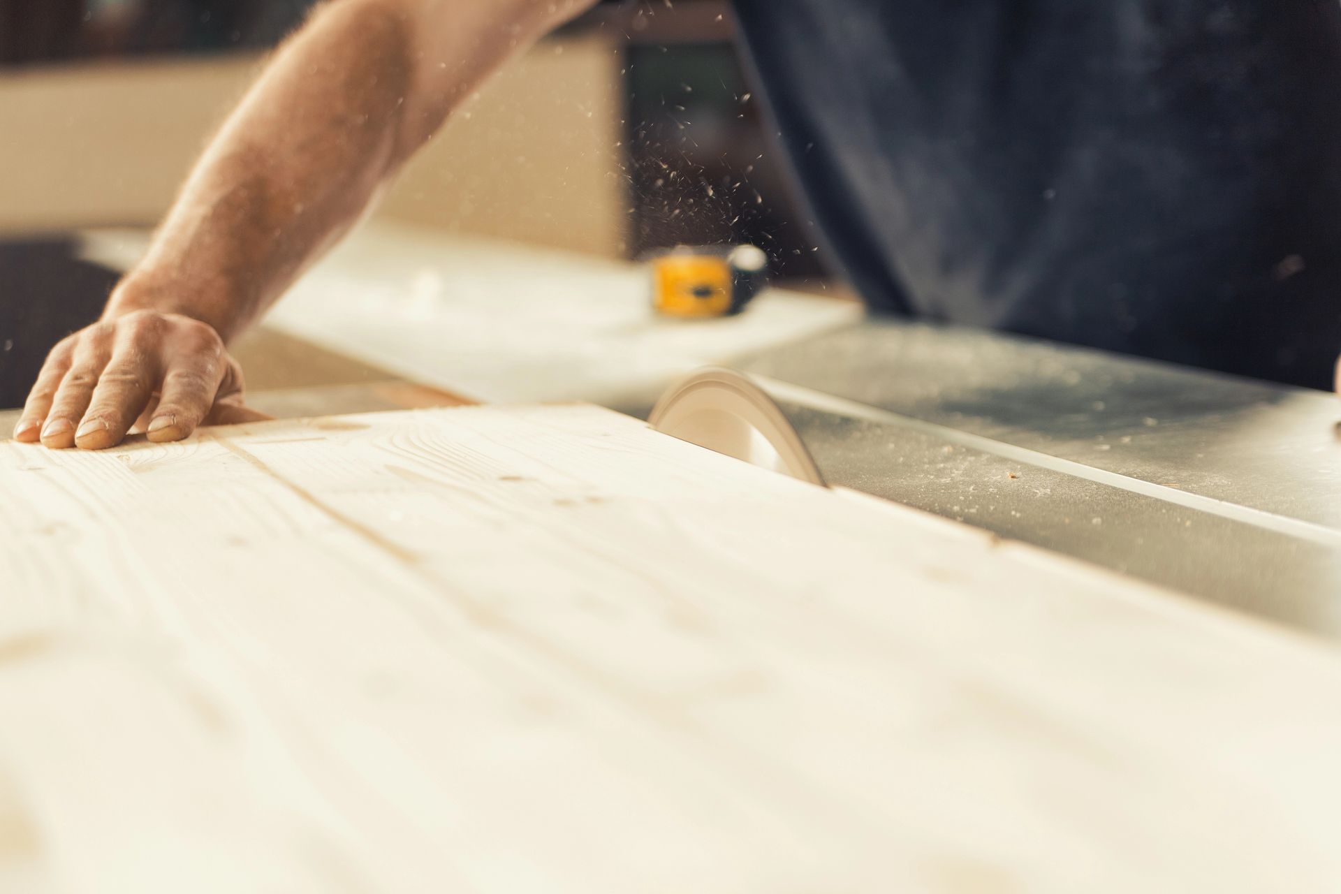 Persona che usa una sega da tavolo per tagliare un'asse di legno, con la segatura che vola.