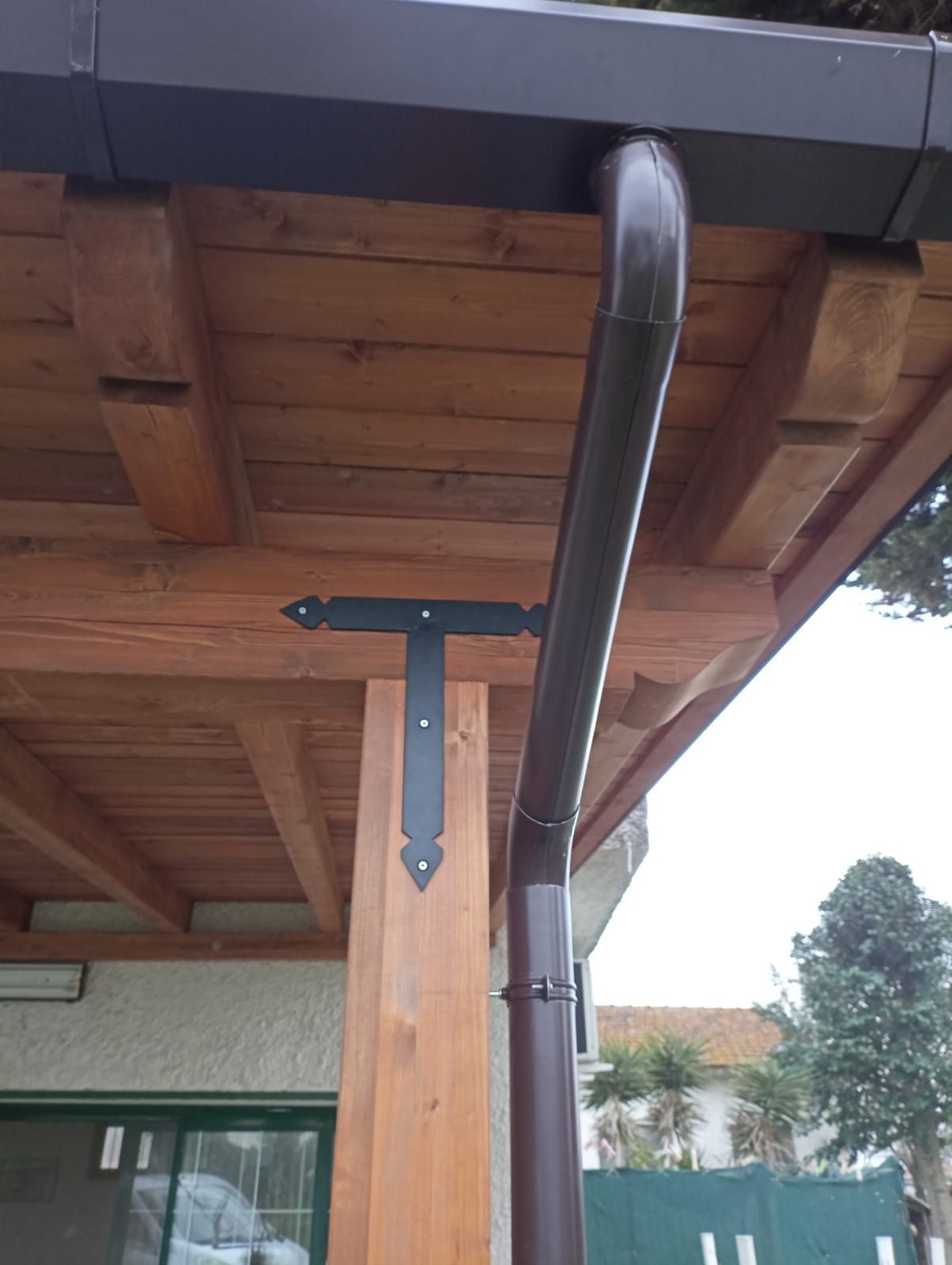 Persona che applica la finitura alle assi di legno del terrazzo con un pennello, indossando guanti e berretto.