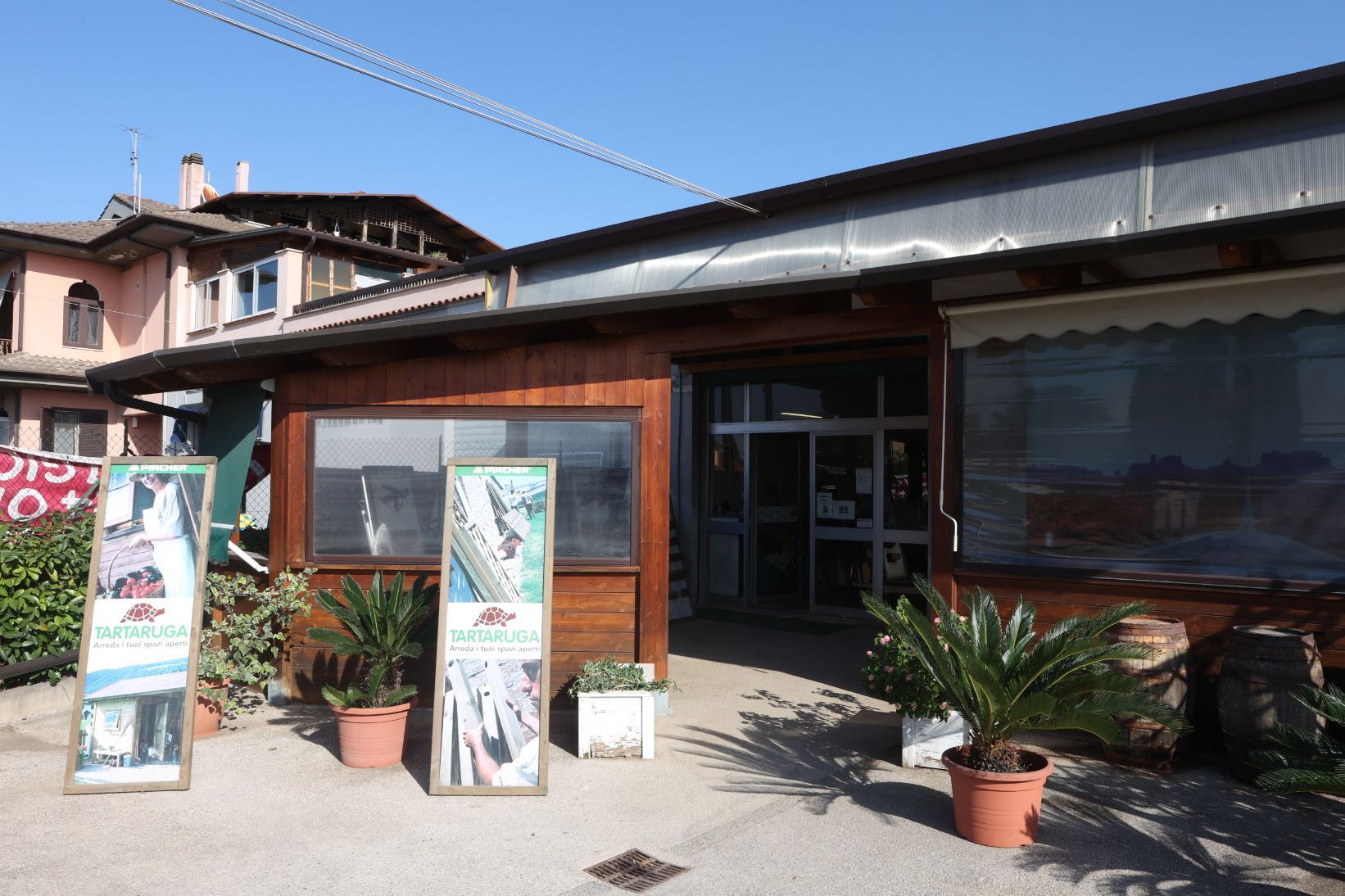 Persona che applica la vernice su una terrazza in legno, indossando cappello, guanti e occhiali.