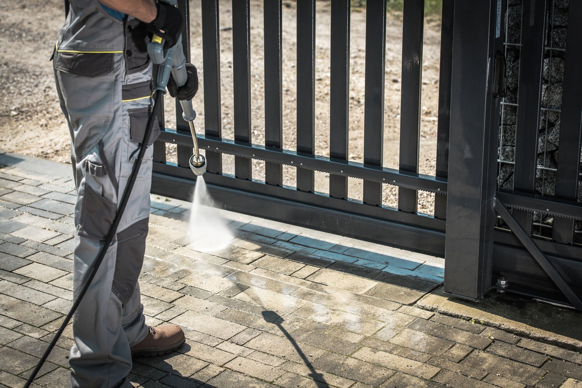 A man is using a high pressure washer to clean a gate.