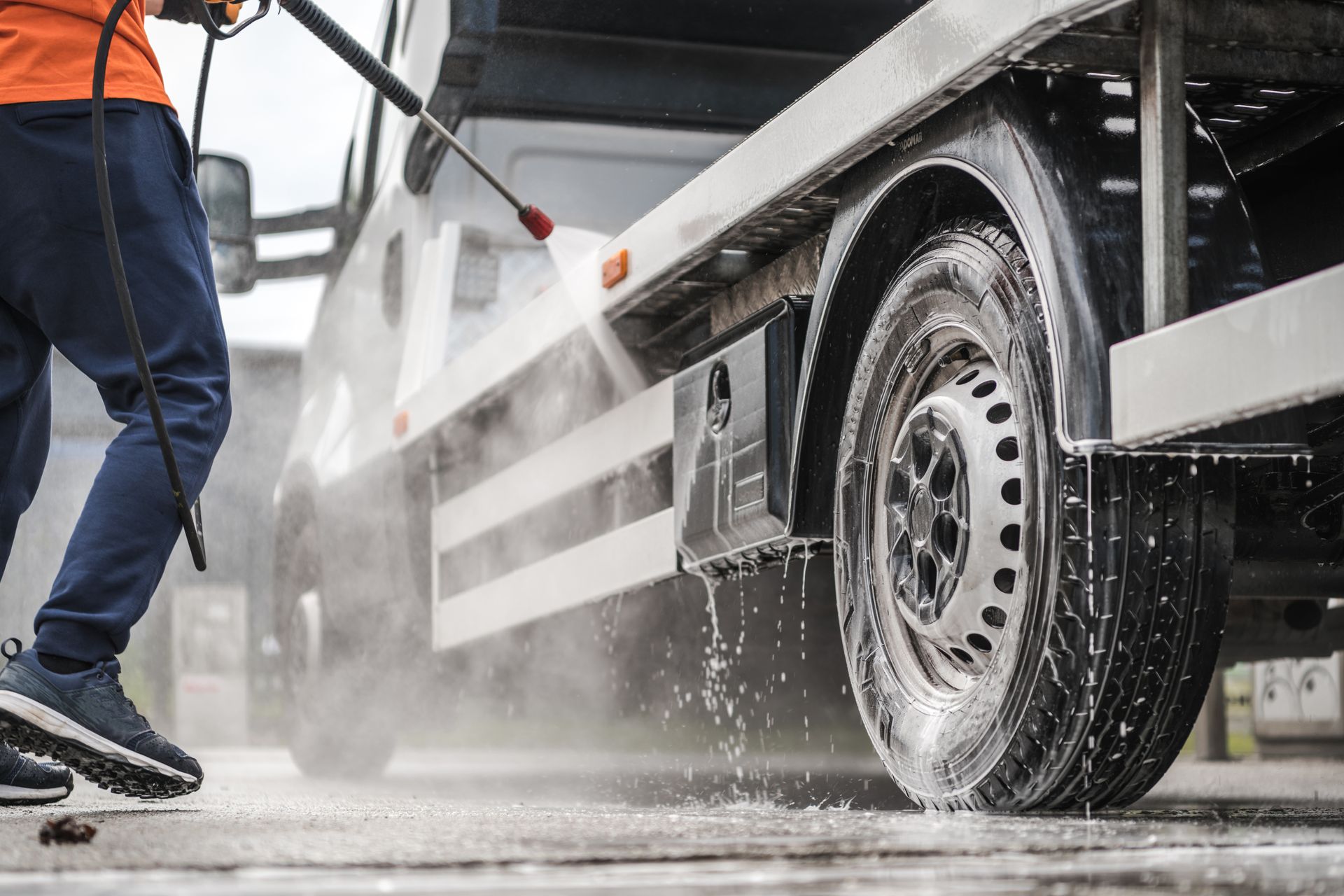 A man is cleaning a truck with a high pressure washer.