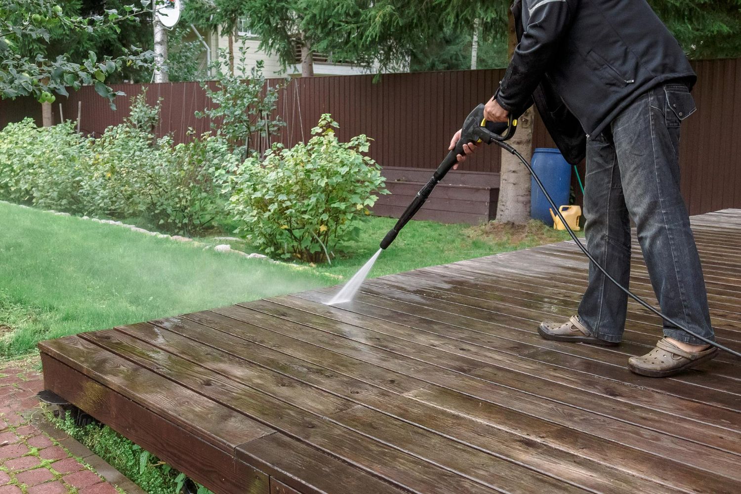 A man is using a high pressure washer to clean a wooden deck.