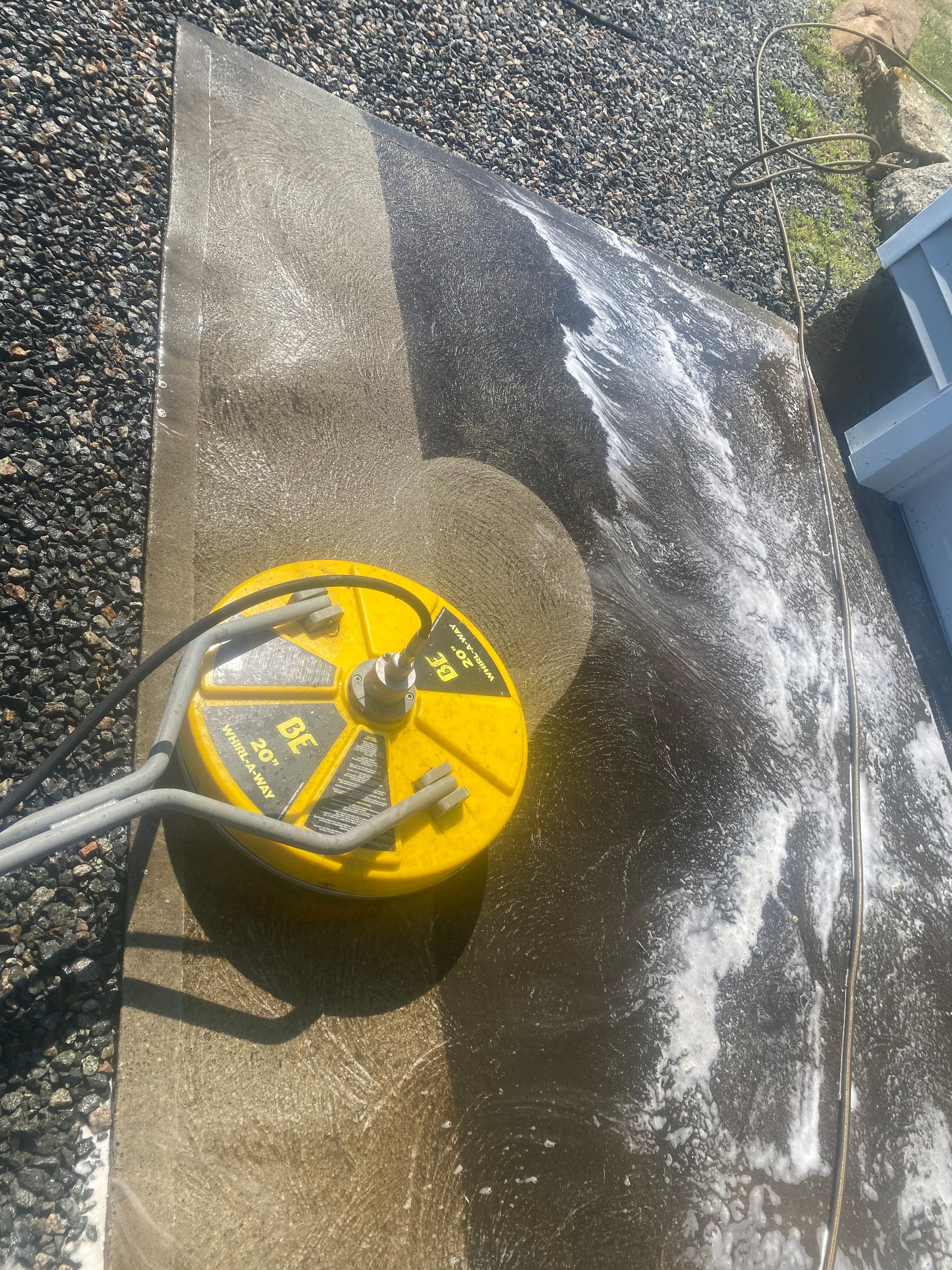 A yellow pressure washer is being used to clean a concrete surface.