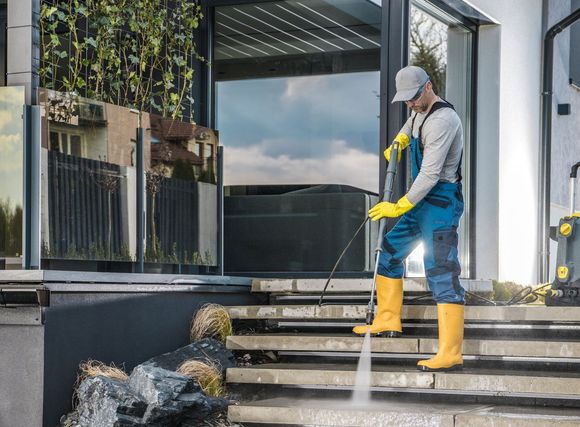 A man is cleaning the steps of a building with a high pressure washer.