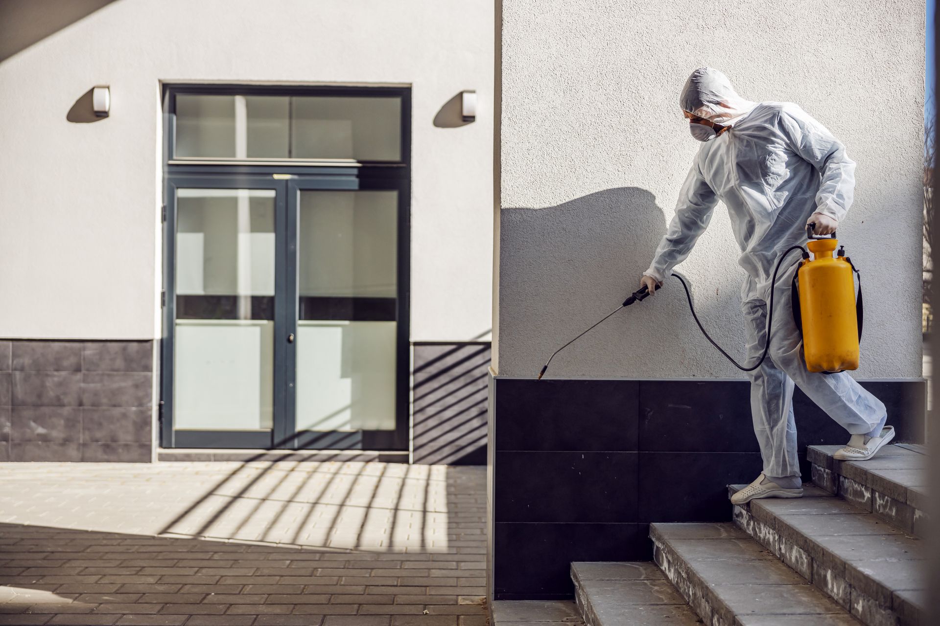 A man in a protective suit is spraying a wall with a sprayer.