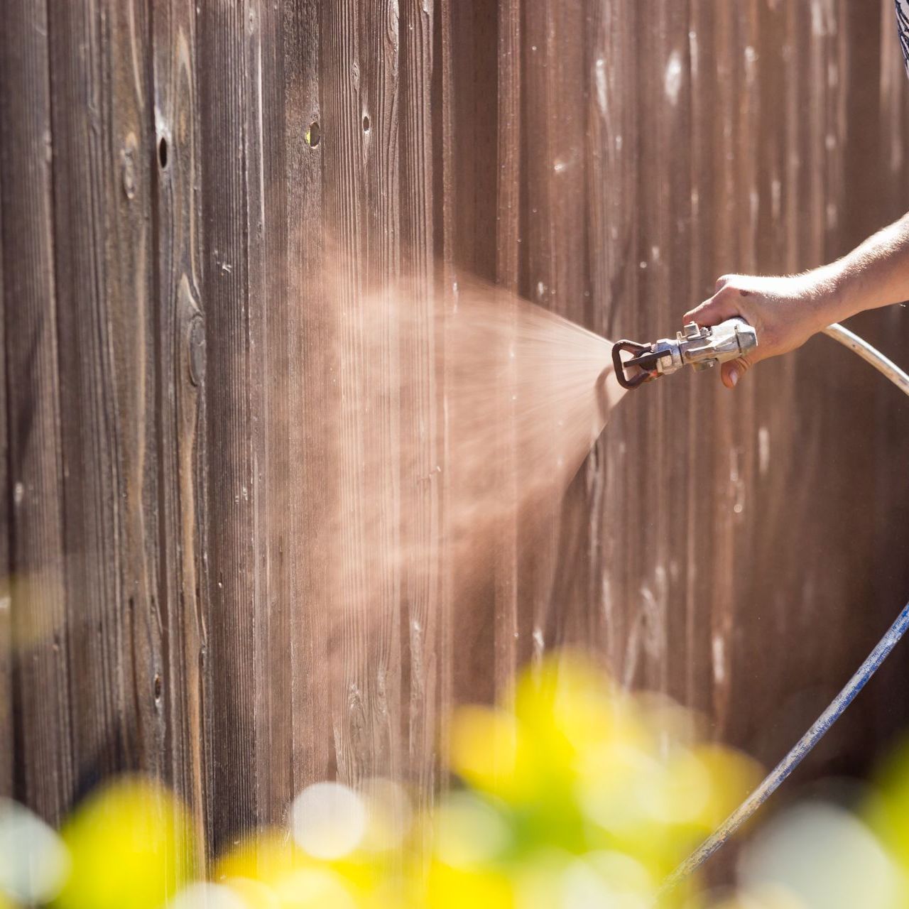 A person is spraying a wooden fence with a hose.