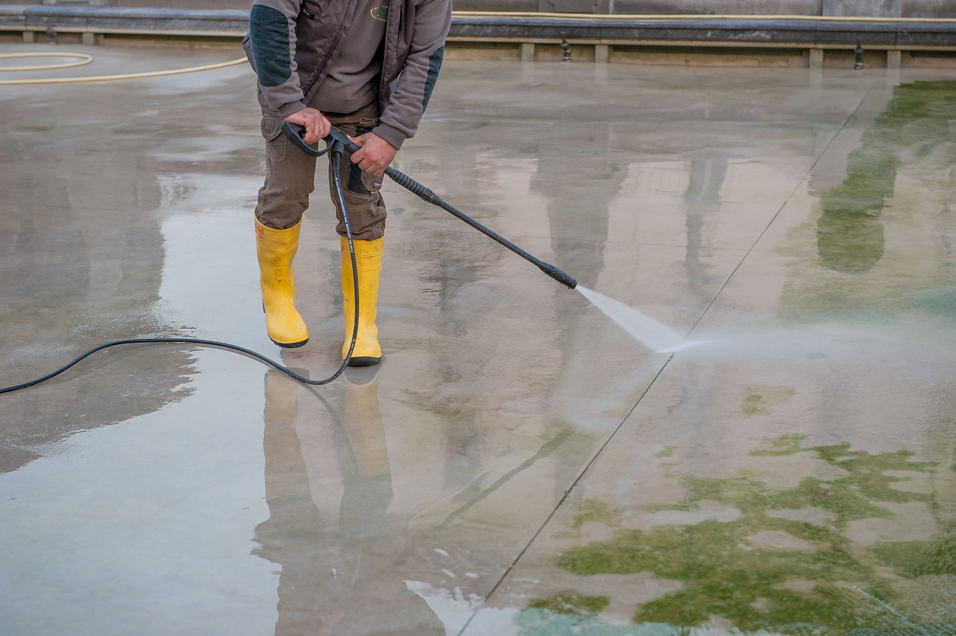 A man is cleaning a sidewalk with a high pressure washer.